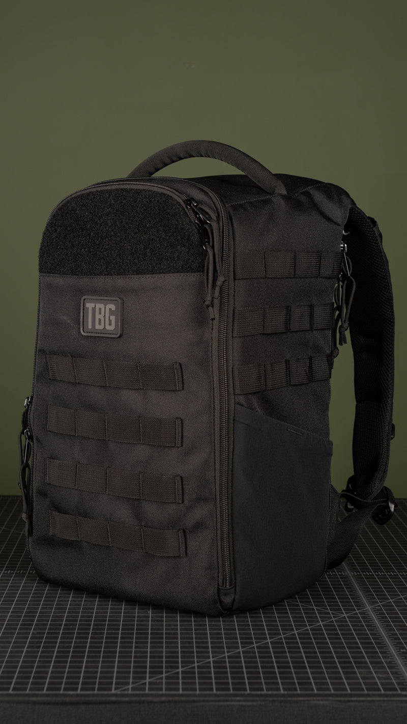 Black tactical diaper bag with MOLLE webbing and TBG logo on a green background.