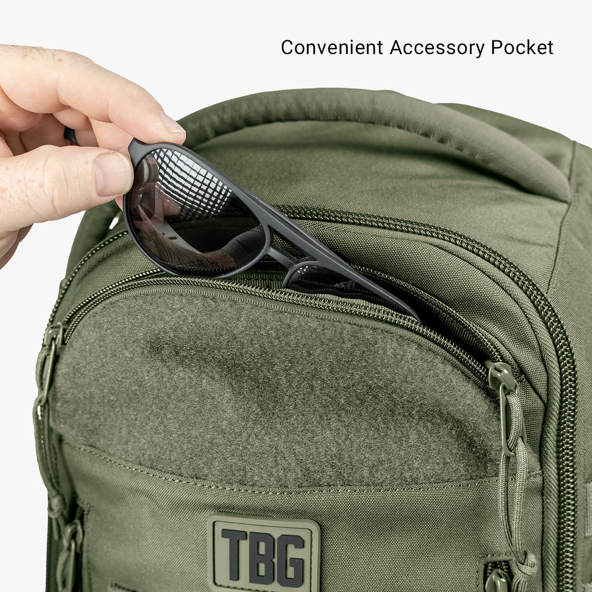 Green tactical diaper bag with a front zippered pocket and a pair of sunglasses being stored in a convenient accessory pocket.