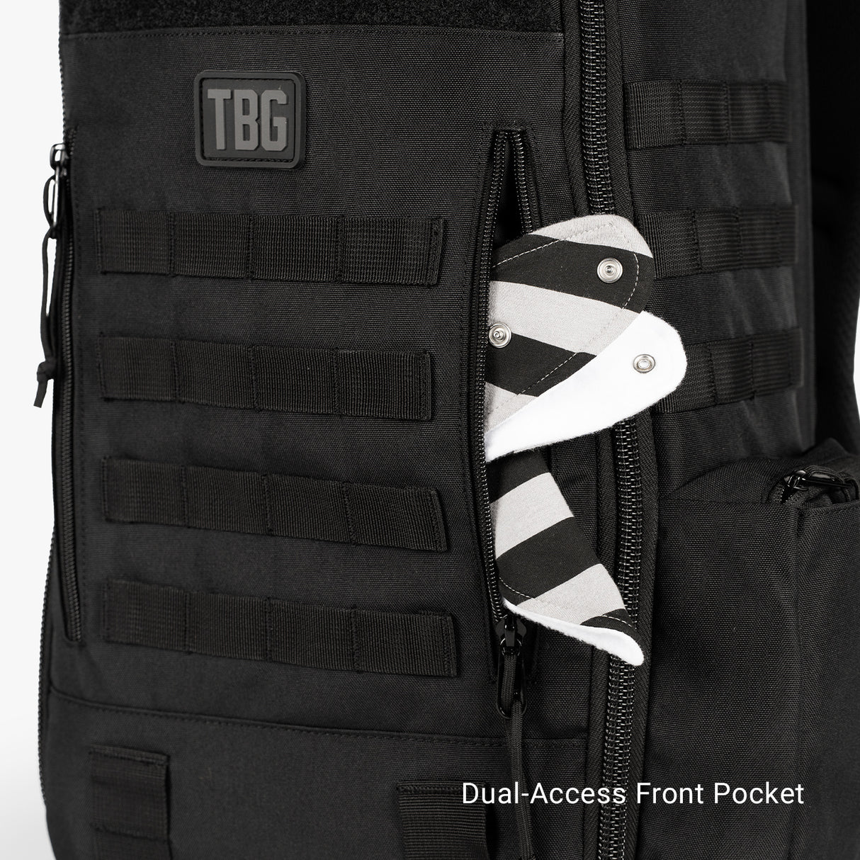 Black tactical daypack with dual-access front pocket holding a striped baby sock, designed for diaper bag and baby carrier bundle.