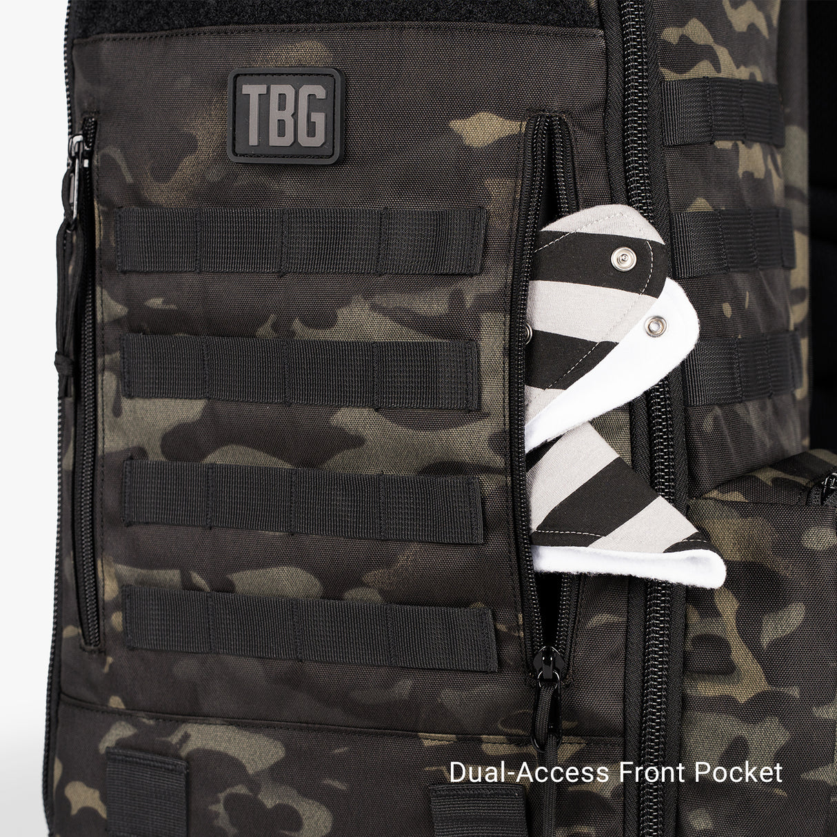 Camo-patterned daypack diaper bag with multiple MOLLE-style straps and a dual-access front pocket, holding a baby sock.