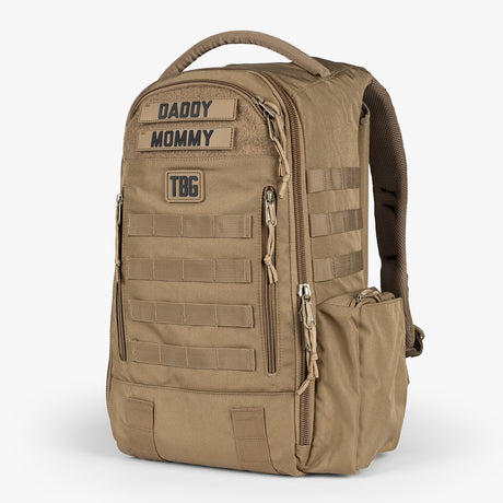 Tactical Baby Gear daypack diaper bag in tan with multiple zippered compartments, MOLLE webbing, and a top handle for easy carrying.