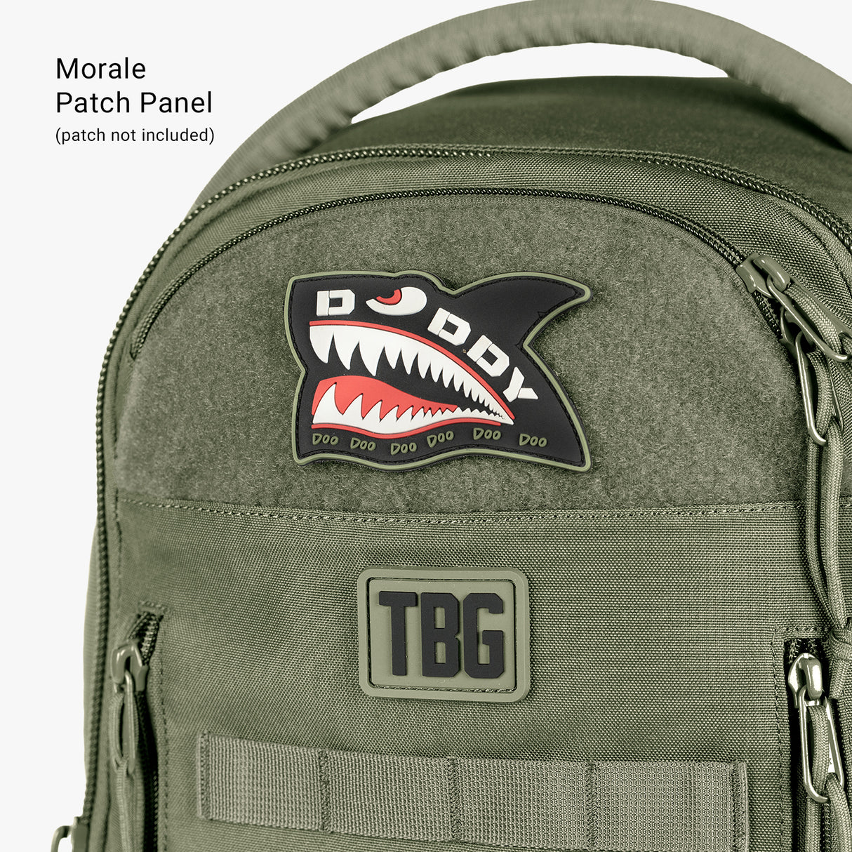 Close-up of a green tactical daypack diaper bag with patches, including a shark design and "TBG" logo, featuring multiple zippered compartments.