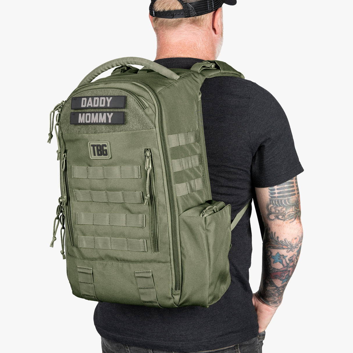 Green tactical daypack diaper bag with baby carrier straps, patches, multiple compartments, and MOLLE webbing.