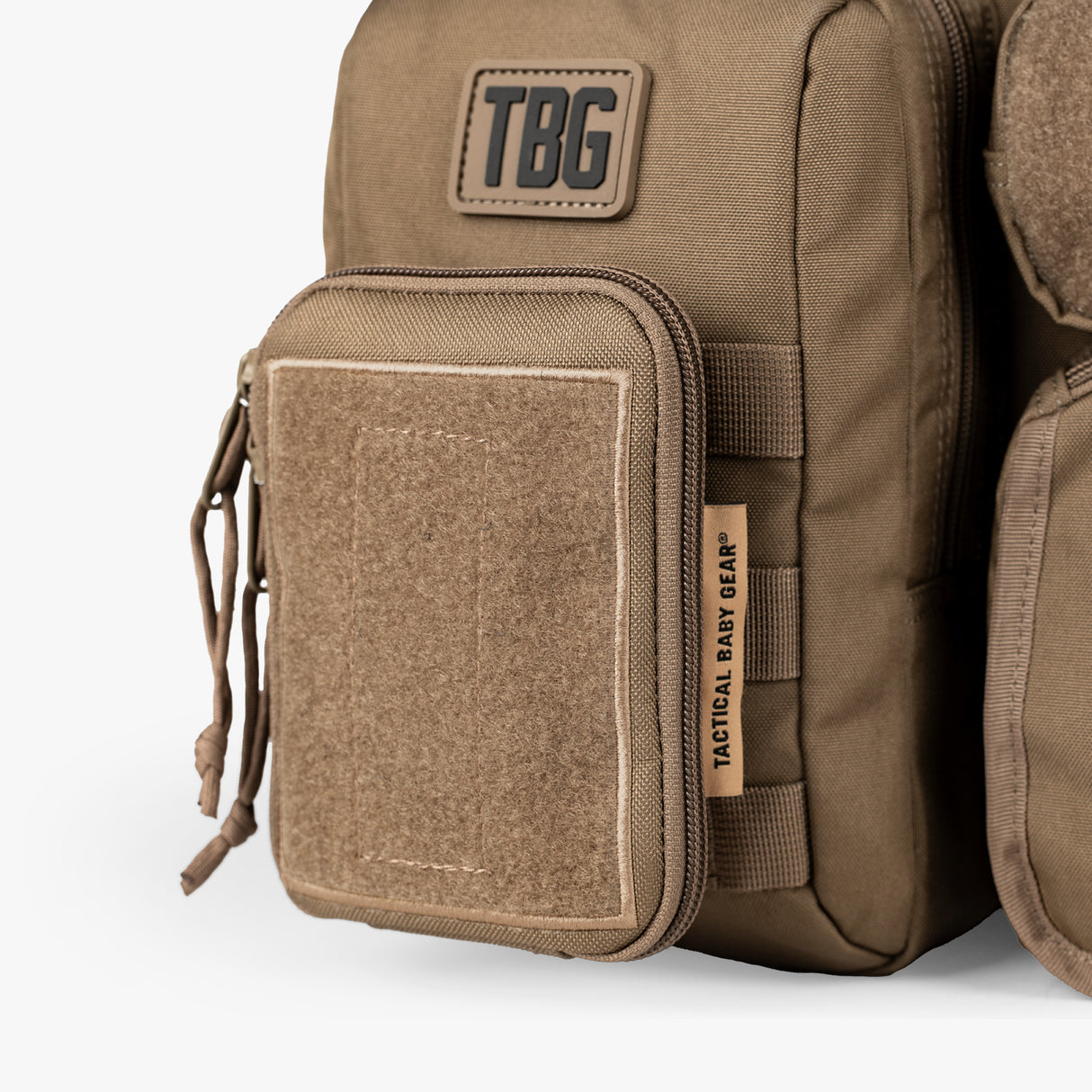 Close-up of a tan tactical diaper bag and baby carrier bundle with a front zippered pocket, Velcro patch, and Tactical Baby Gear branding.
