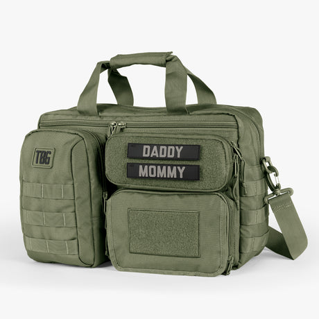 Olive green tactical diaper bag with multiple compartments, Velcro patches labeled Daddy and Mommy, and adjustable shoulder strap.