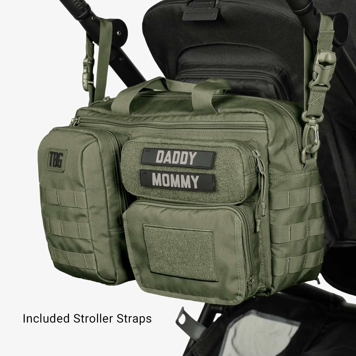 Olive green diaper bag with multiple compartments and patches labeled Daddy and Mommy, attached to a black stroller.