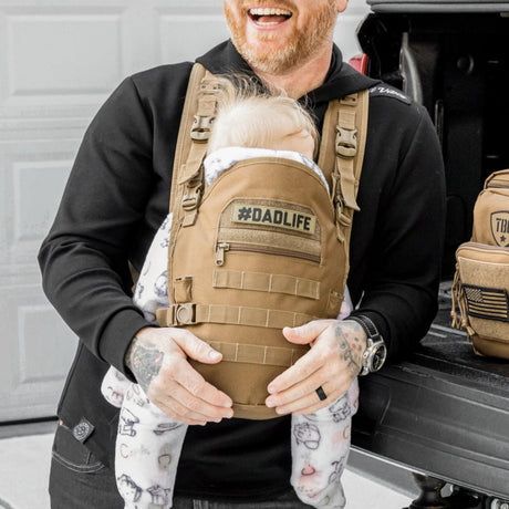 Man holding toddler in a khaki #DADLIFE tactical baby carrier.