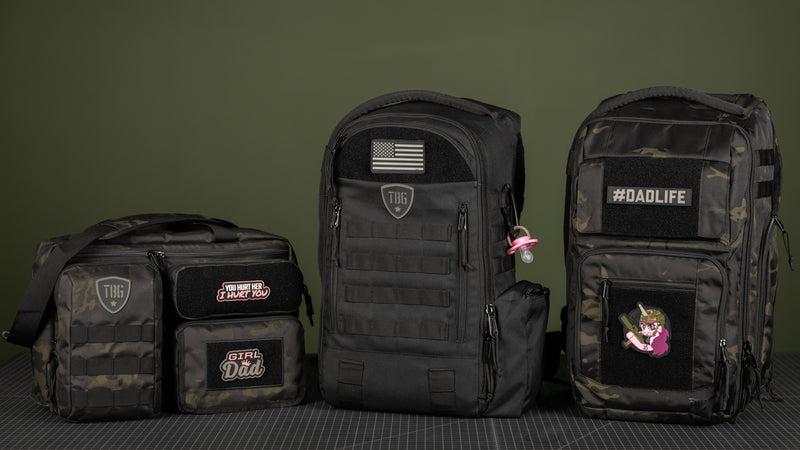 Three black tactical bags with camouflage accents displayed on a grid surface, featuring custom patches such as “Girl Dad,” “You Hurt Her I Hurt You,” and “#DADLIFE,” with an olive-green background.
