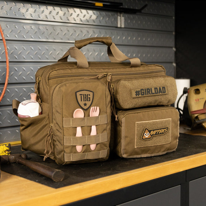 Olive green tactical diaper bag with patches, set on a workbench.