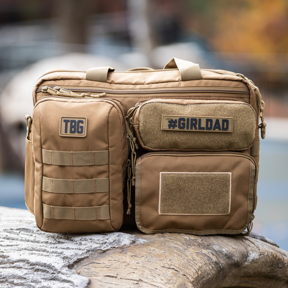 Tactical Baby Gear #GIRLDAD name tape patch on a rugged tan diaper bag with multiple compartments and patches.