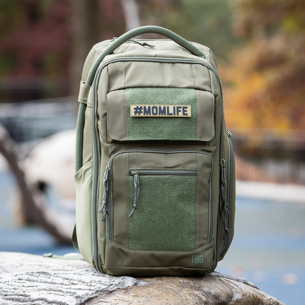 Olive green tactical backpack featuring a "#MOMLIFE" name tape PVC patch, designed for rugged parenting.