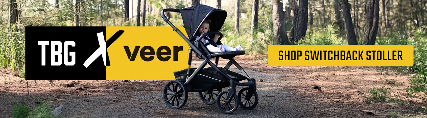 Black and gray tactical stroller with a baby, on a forest path, with TBG and Veer logos.