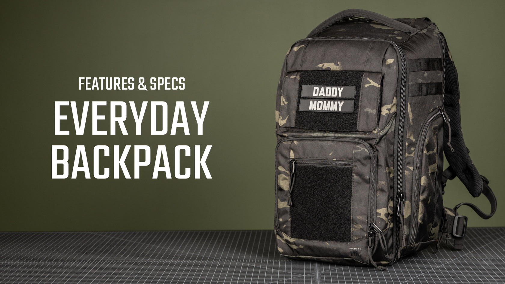 Black and camouflage diaper backpack with "DADDY MOMMY" patch, displayed on a green background.