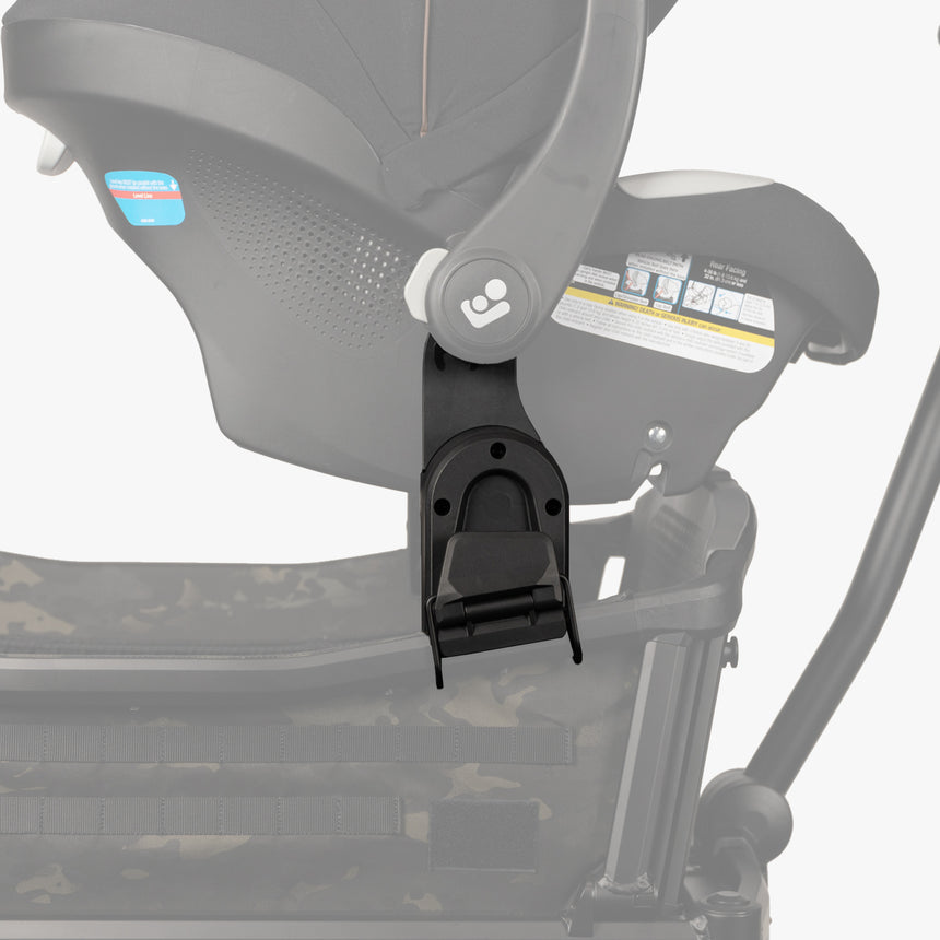 Alt text: "Close-up of a gray Maxi-Cosi car seat adapter attached to a stroller frame, showing detailed safety labels and secure locking mechanism."
