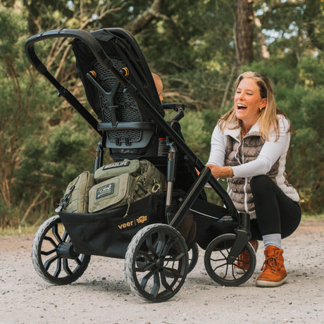 Military-inspired, rugged stroller with black frame, large wheels, and tan storage bags, perfect for adventurous parents.