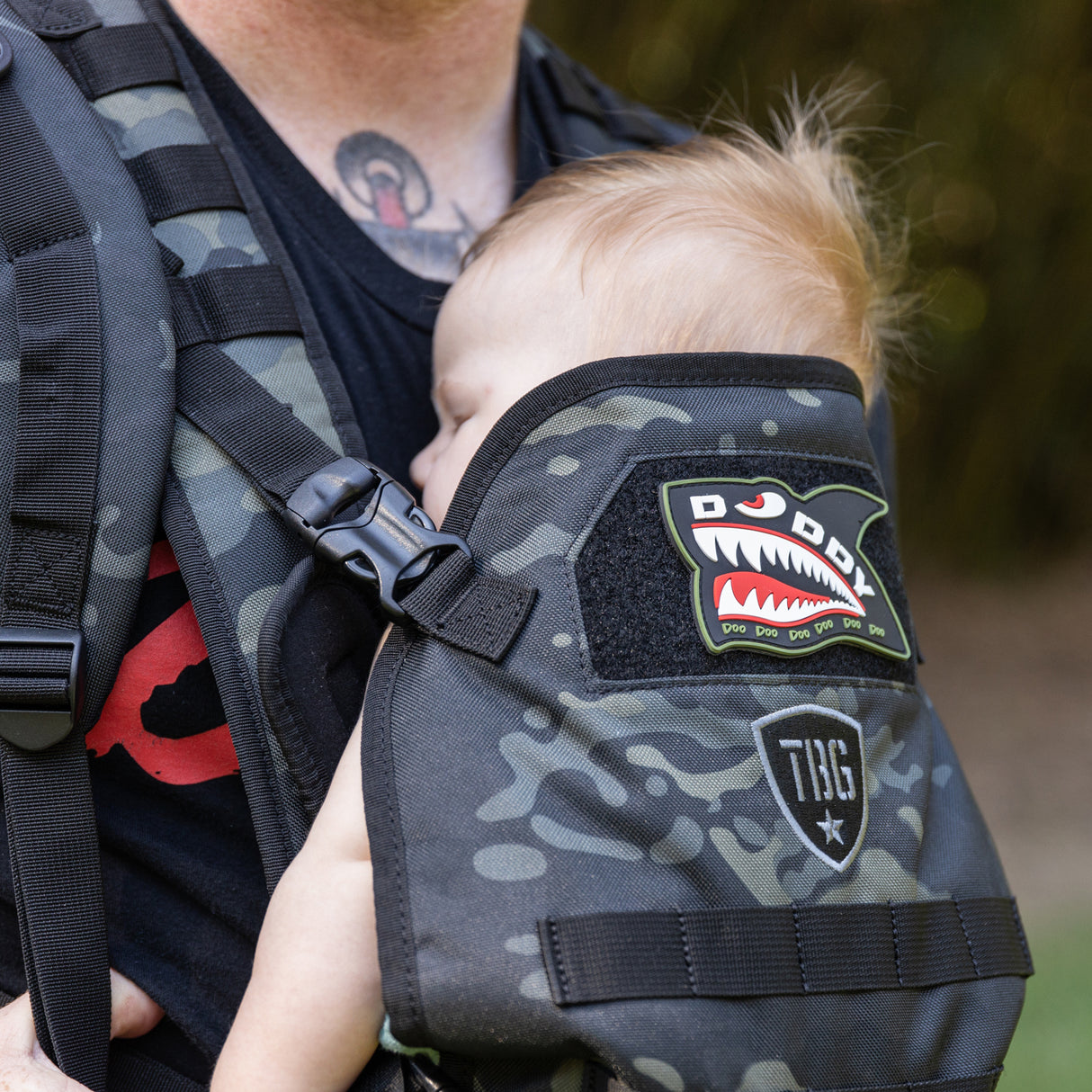 Baby asleep in black camo baby carrier. Daddy Shark patch is attached to carrier.