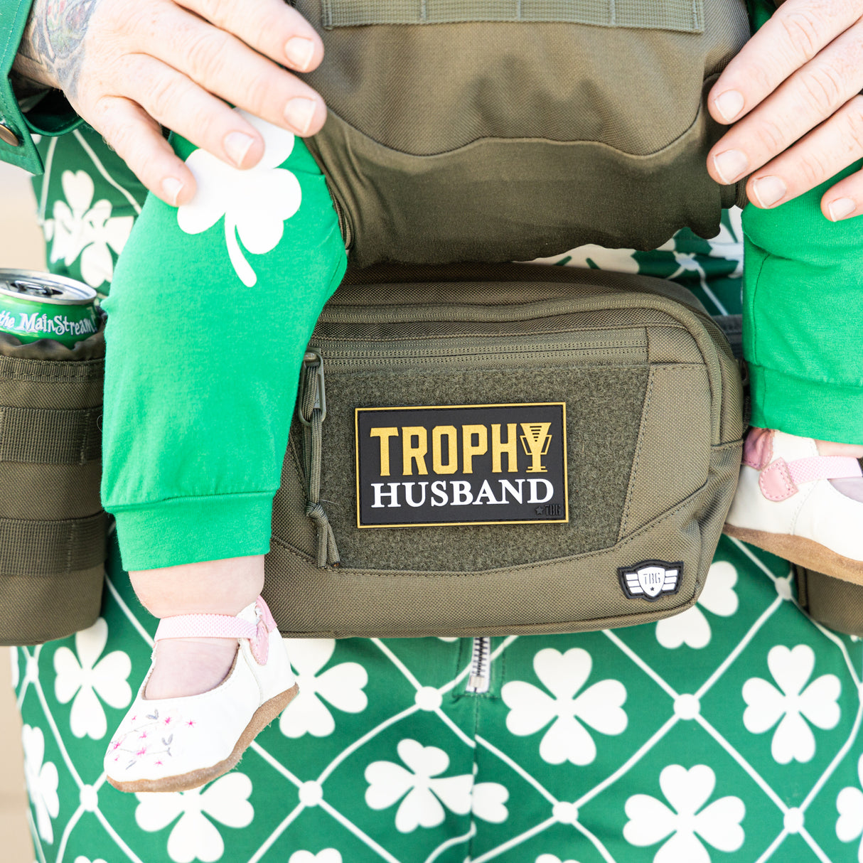 Trophy Husband patch on green fanny pack worn beneath baby carrier with baby in it.