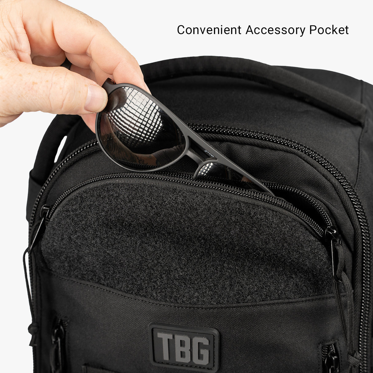 Hand placing sunglasses into the convenient accessory pocket of the Tactical Baby Gear Daypack Mini + Mat.