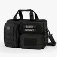 Black tactical diaper bag with multiple compartments, Velcro patches labeled Daddy and Mommy, and a detachable shoulder strap.
