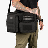 Rugged black Deuce Diaper Bag with adjustable strap, featuring patches labeled "DADDY" and "MOMMY" for modern parents.