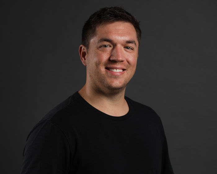 Smiling man wearing a black, rugged tactical t-shirt against a gray background.