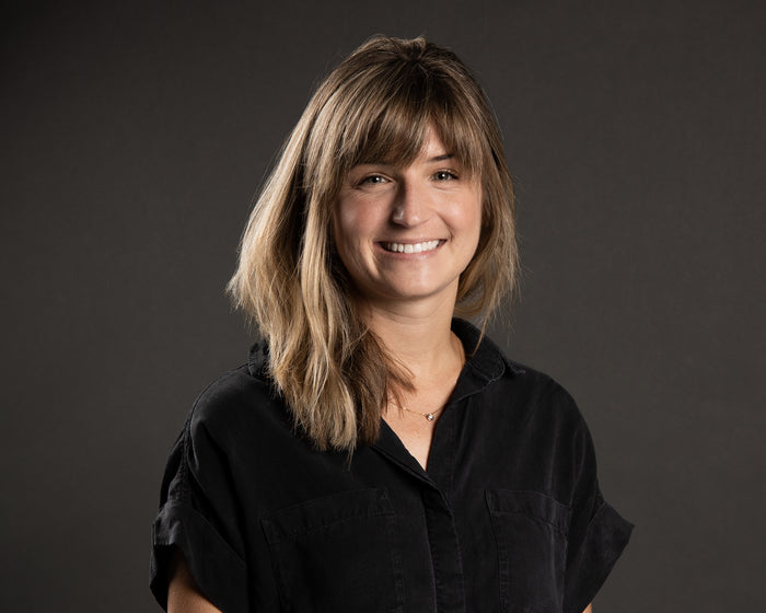 Woman in black, military-style shirt smiling against a gray background.