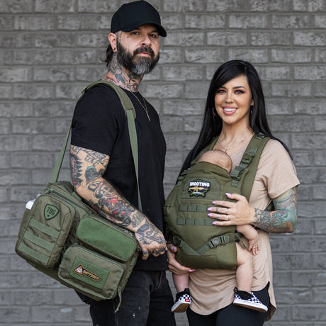 man and women with baby. Dad holding a diaper bag. Mom wearing baby in a baby carrier