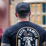 Man wearing a black t-shirt with 'Faith, Family, Freedom' design in an outdoor setting.