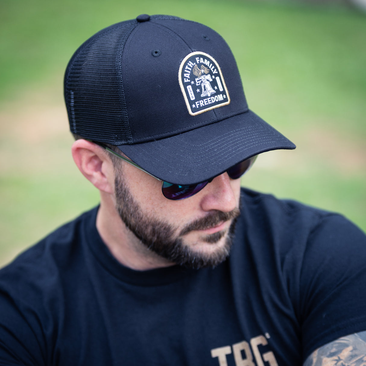 Man wearing a black Faith Family Freedome hat and sunglasses, sitting outdoors.