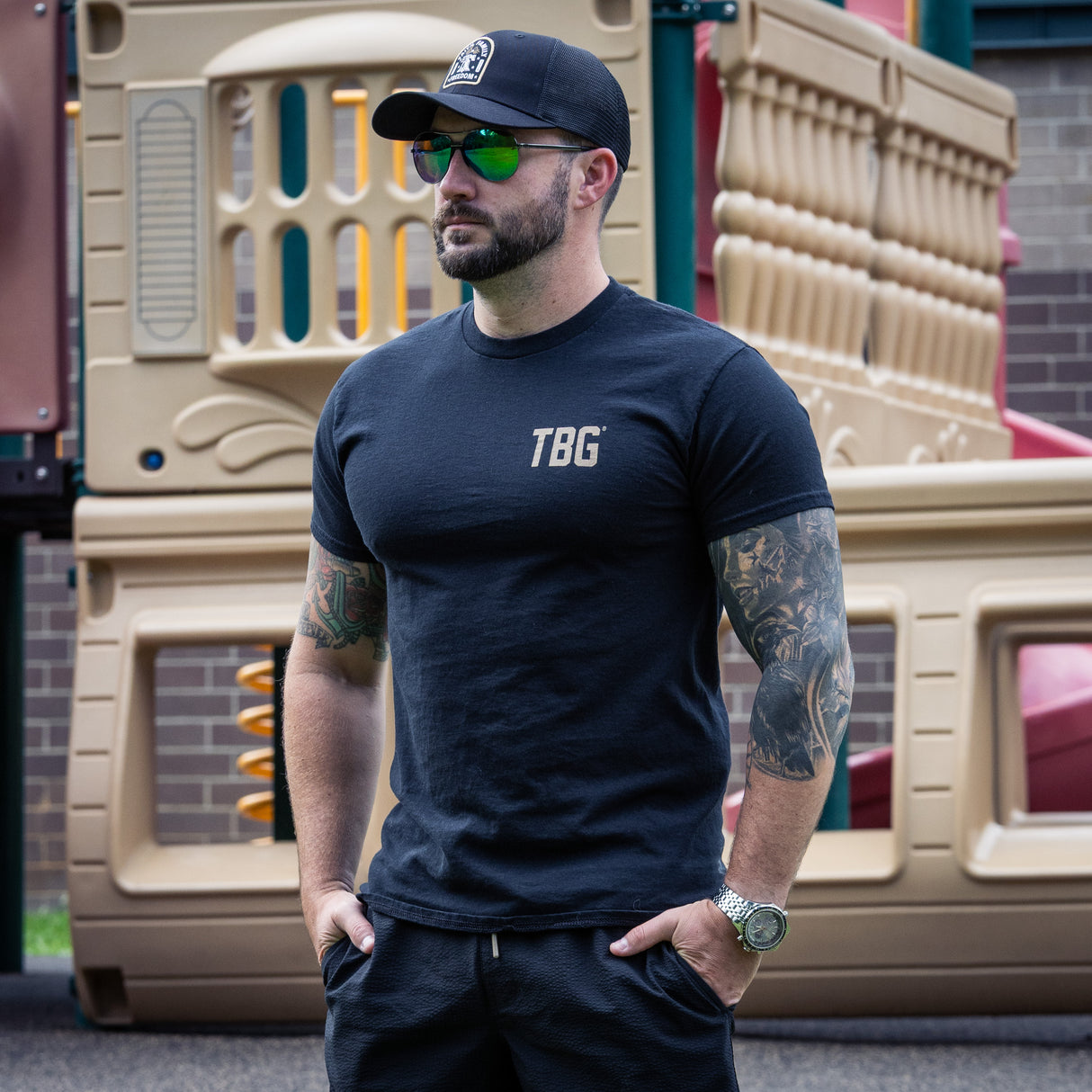 Man wearing a navy 'TBG' t-shirt in front of a playground.