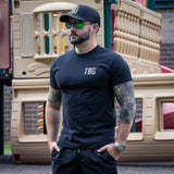 Man wearing a navy 'TBG' t-shirt in front of a playground.
