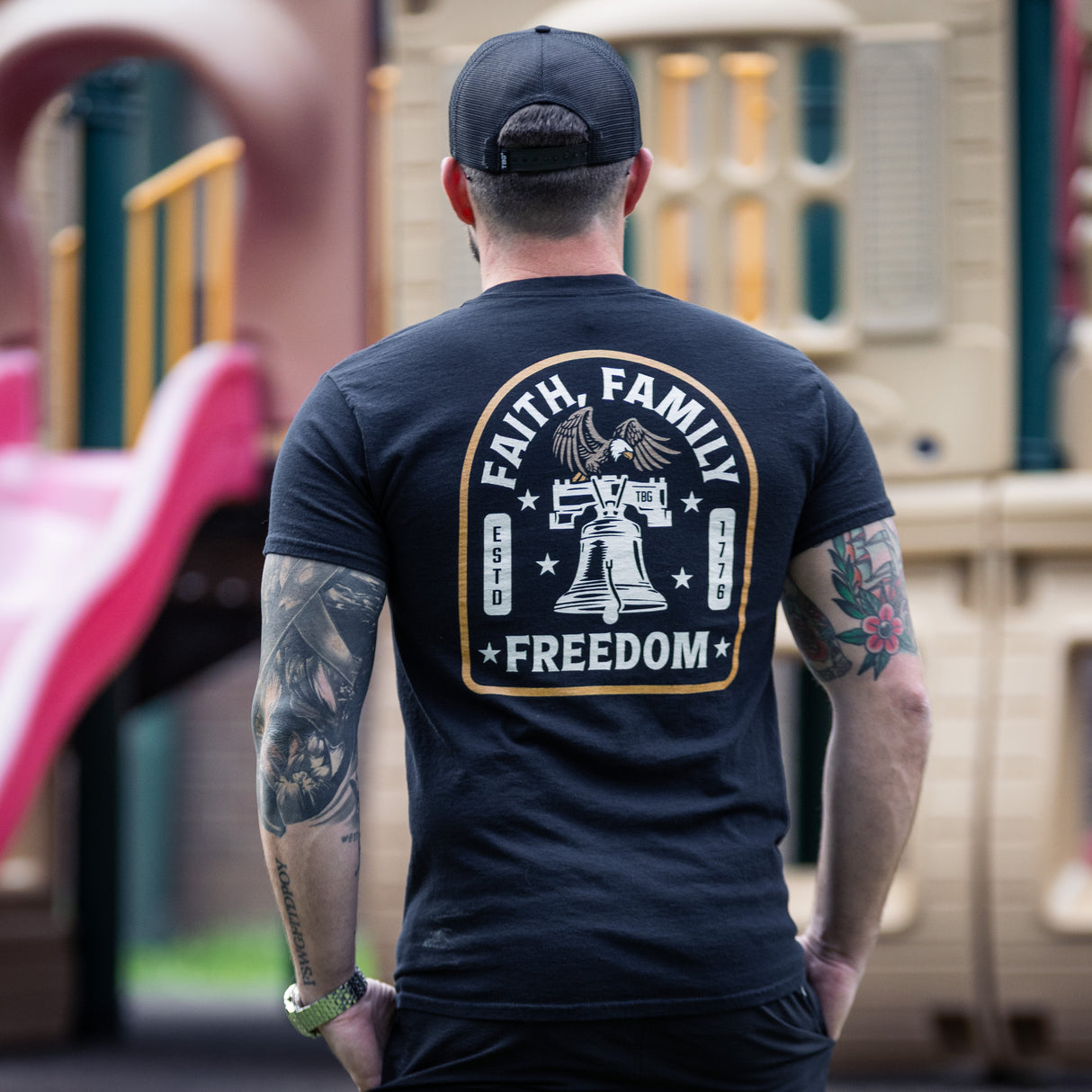 Man wearing a black t-shirt with 'Faith, Family, Freedom' design in an outdoor setting.