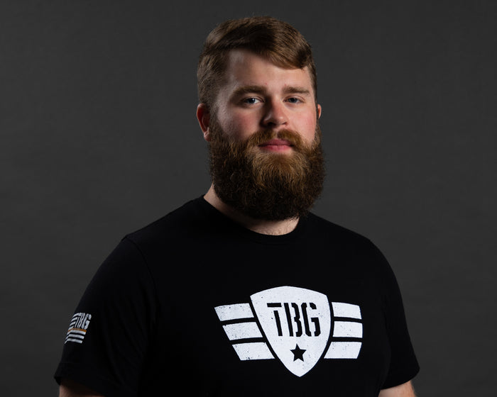 Man in black military-inspired T-shirt with bold white and gray logo.