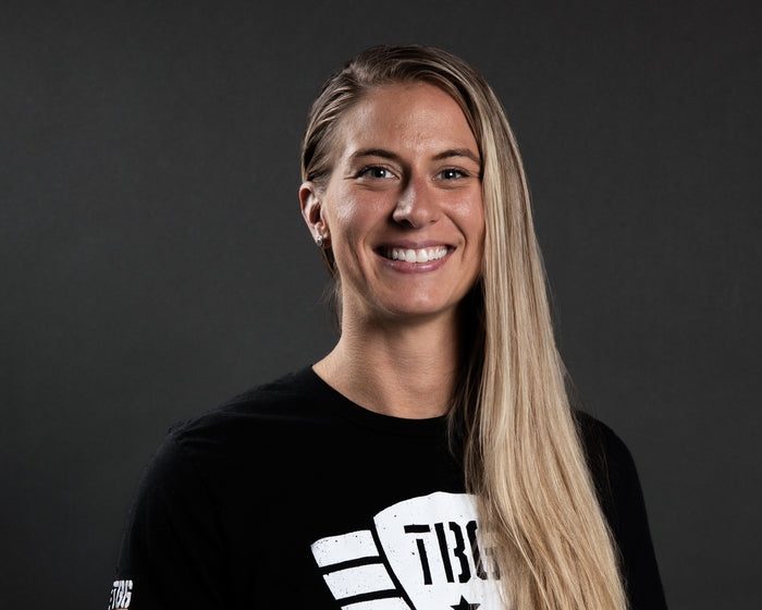 Woman in black T-shirt with bold white logo, smiling, against a dark background.