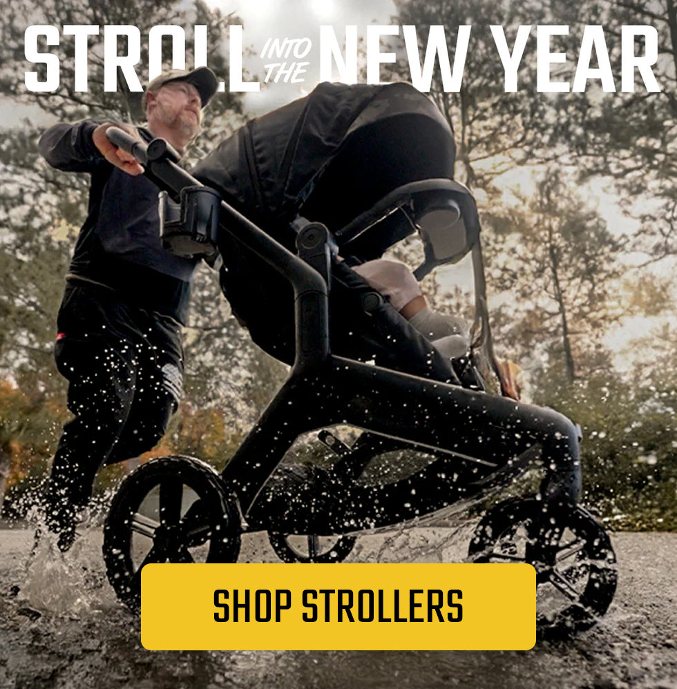 Man pushing a black stroller through a puddle on a forest path, with text reading “Stroll Into the New Year” and a yellow button labeled “Shop Strollers.”