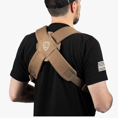 Man wearing a khaki tactical baby carrier with crossed shoulder straps and logo patch.
