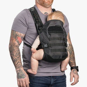 Man wearing black baby carrier with infant facing in