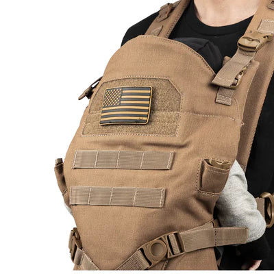 Tan military-style baby carrier with American flag patch, worn by a person in a black shirt.