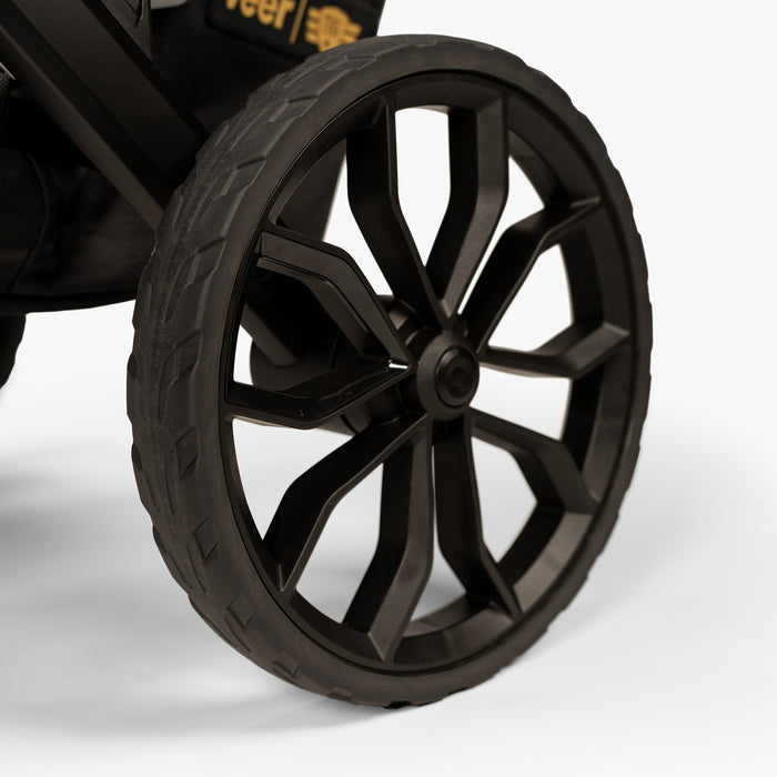 Close-up image of a rugged stroller wheel from the TBG Veer Switchback Newborn Bundle, showing its tread and suspension detail.