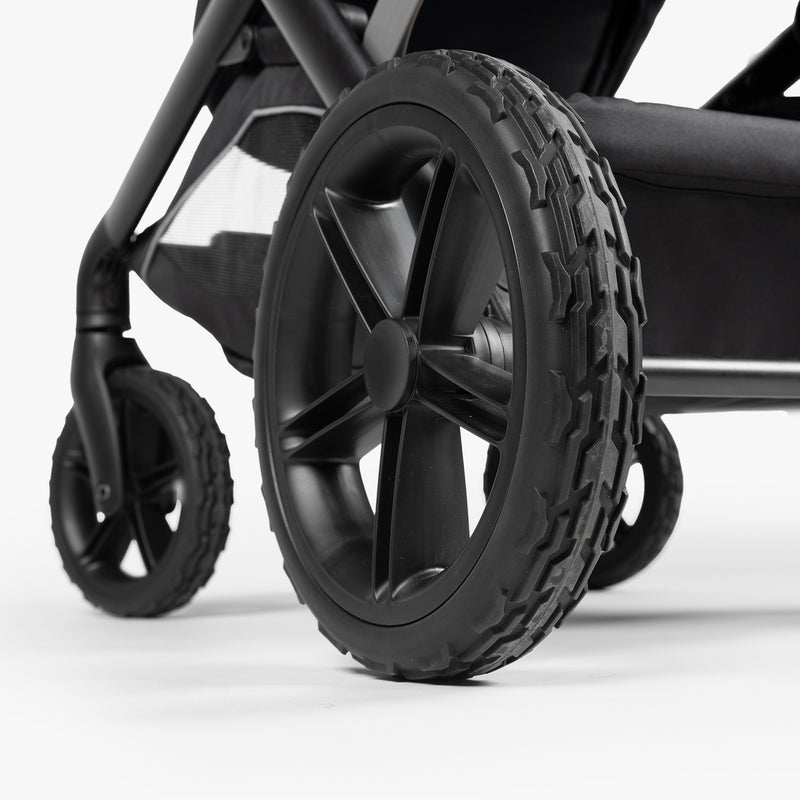 Close-up of rugged black stroller wheels with thick treads, designed for outdoor, military-inspired parenting gear.