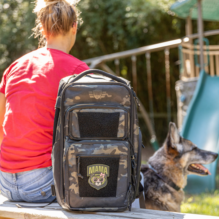 Green Mama Bear face on black camo bag. A woman in a red shirt sits next to the bag.