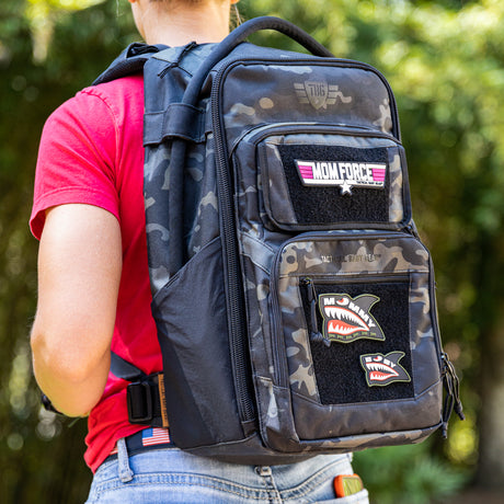 Woman in red shirt wearing black camo backpack with Mommy Shark patch on it. 