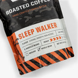 Rugged black and orange coffee bag labeled "Sleep Walker," handcrafted, whole bean, strong, smooth, non-acidic, U.S. roast.