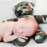Sleeping baby cuddling with camouflage teddy bear.