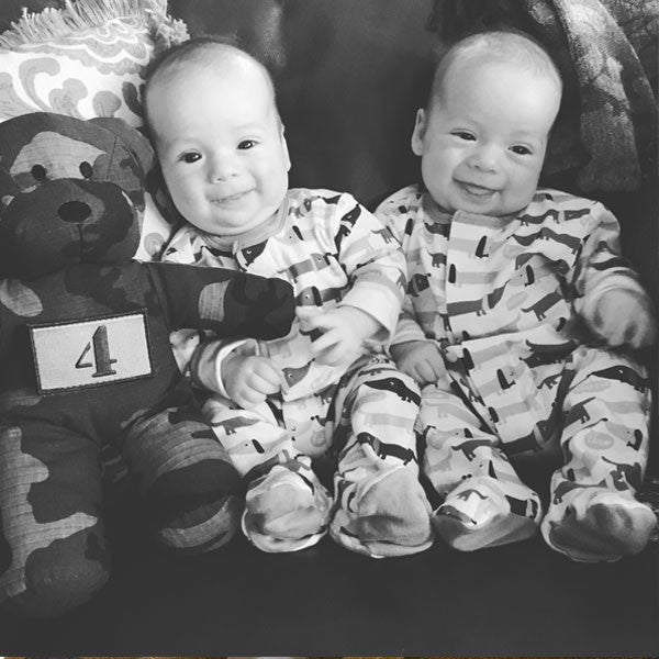 Black and white picture of twin infants cuddling with Tactical Teddy®f