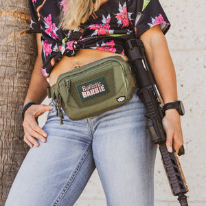 Ballistic barbie patch on green fanny pack worn by woman holding a rifle.