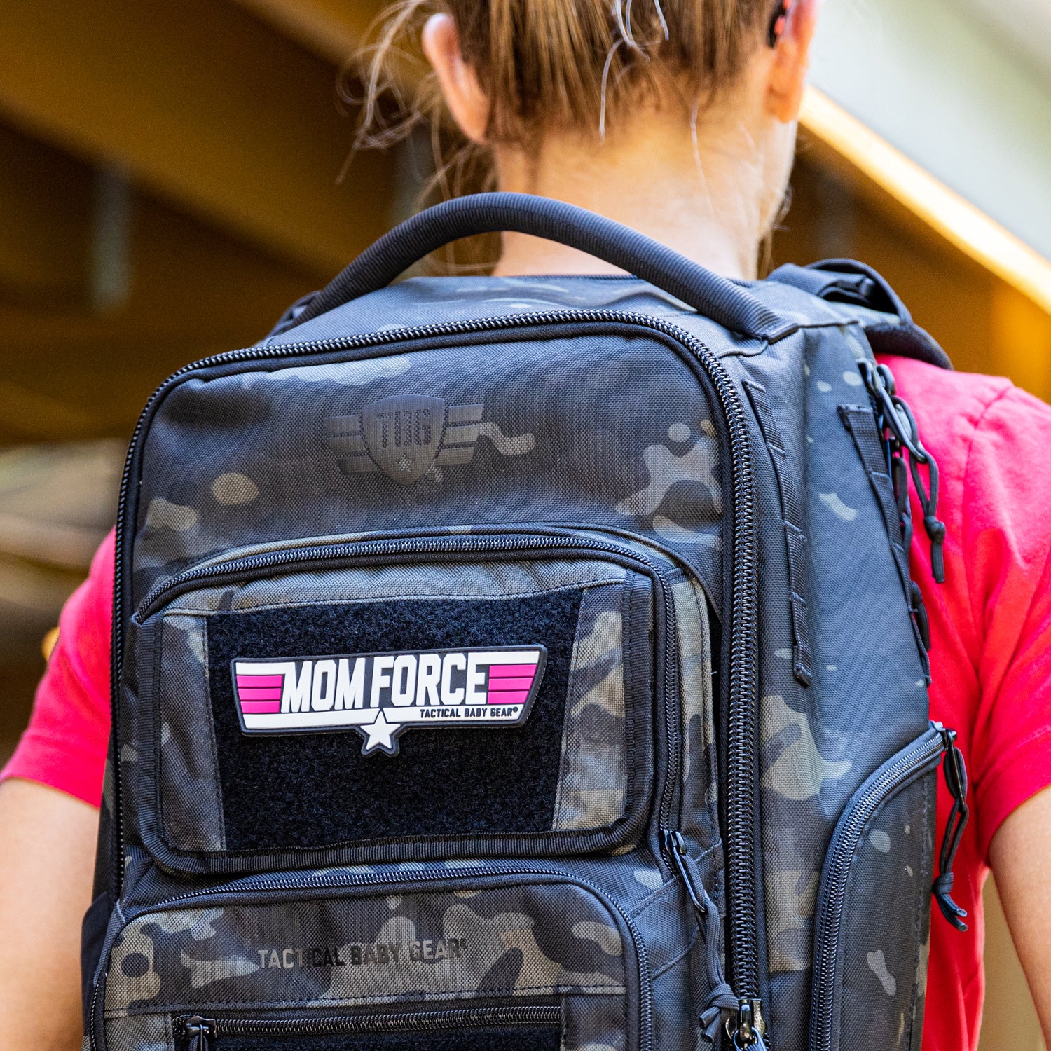 Mom Force patch on black camo backpack worn by white woman. 