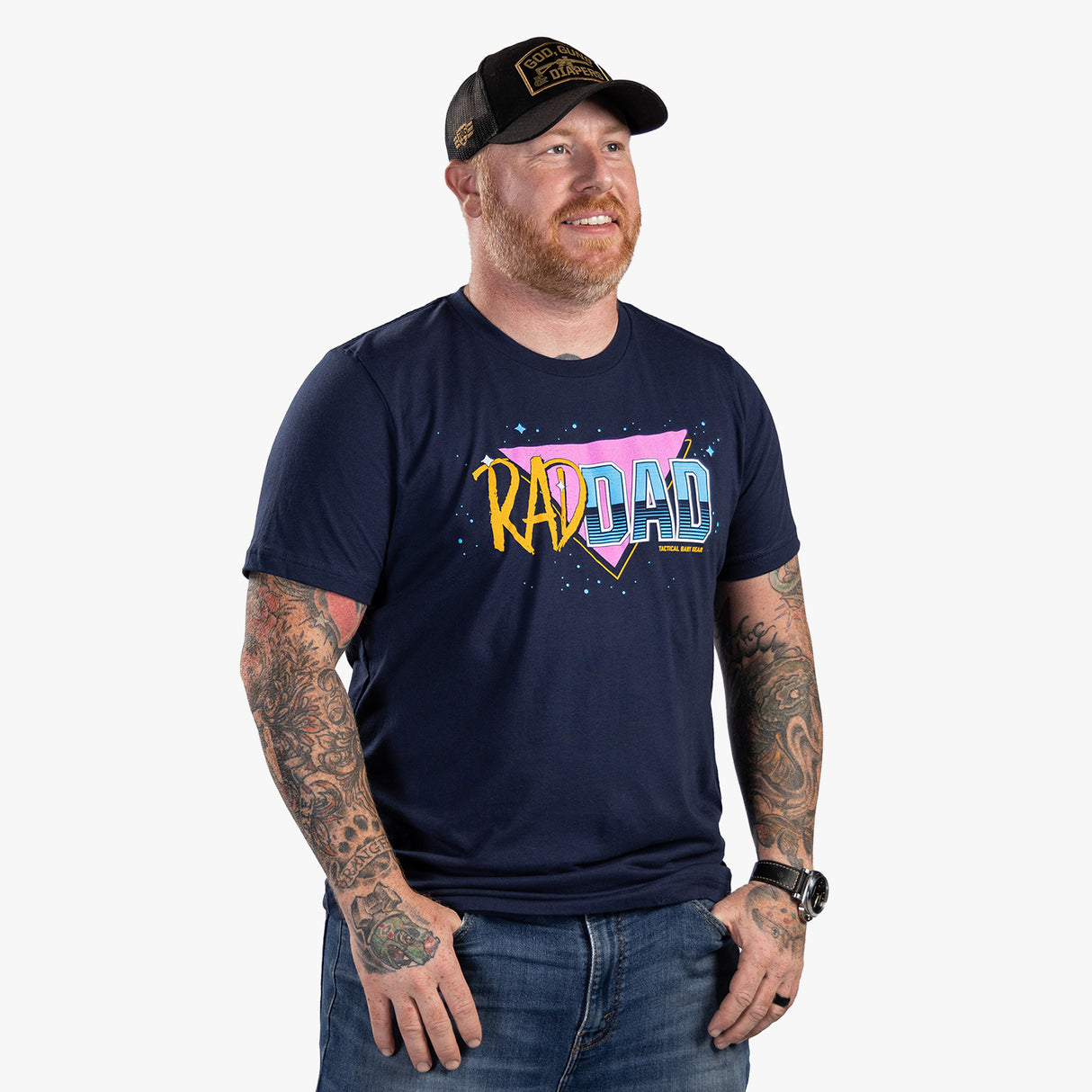 Men's navy T-shirt with colorful "RAD DAD" graphic, tattooed arms, and a black trucker hat with military-inspired patch.