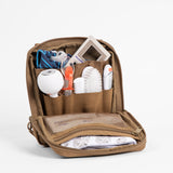 Rugged tan parenting organizer with multiple compartments holding baby essentials like a thermometer, brush, socks, and toys.